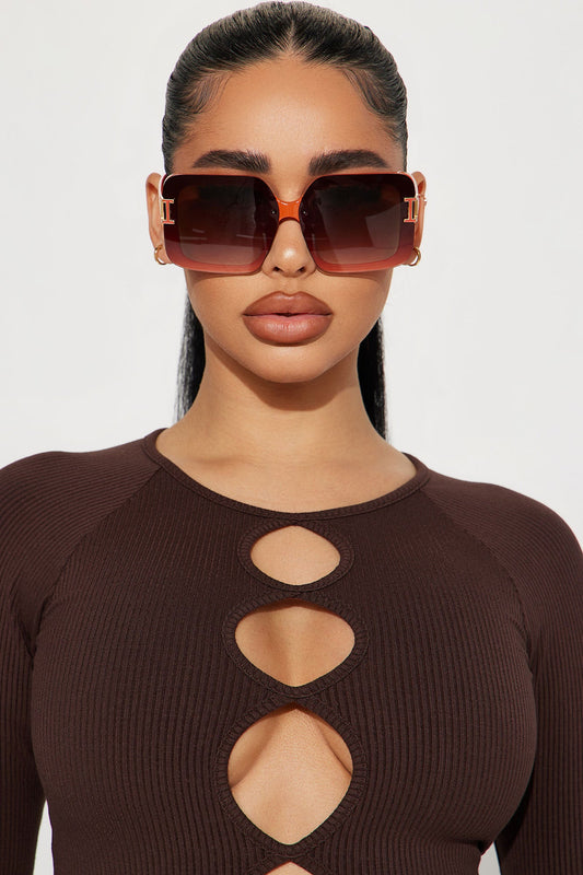 Woman wearing a brown cut-out top and sunglasses against a white background
