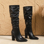 Pair of black knee-high boots on a textured beige background