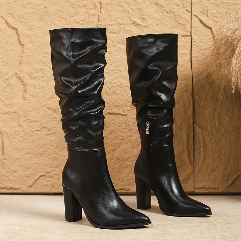 Pair of black knee-high boots on a textured beige background