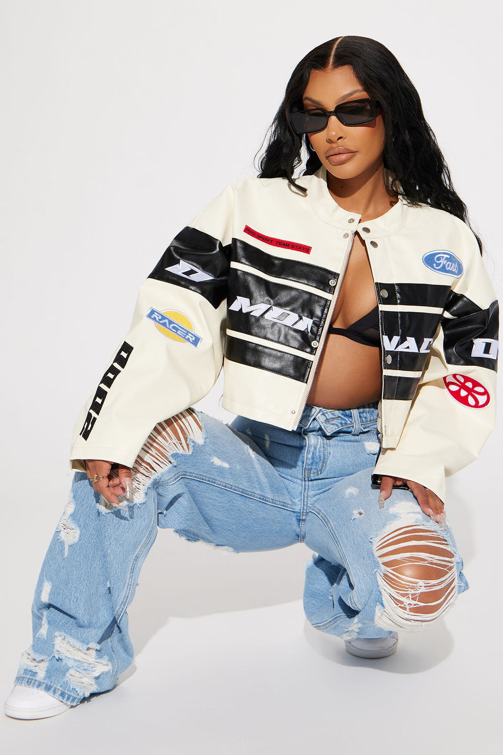 Person wearing a black and white jacket with logos and ripped jeans on a white background