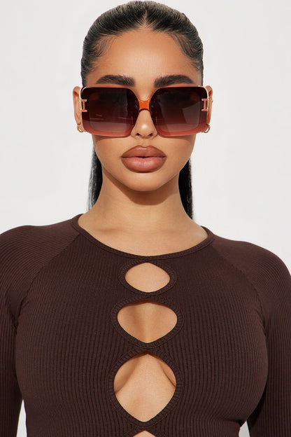 Woman wearing a brown cut-out top and sunglasses against a white background