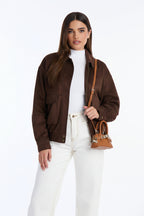 Woman wearing a brown jacket and white pants, holding a brown handbag on a white background