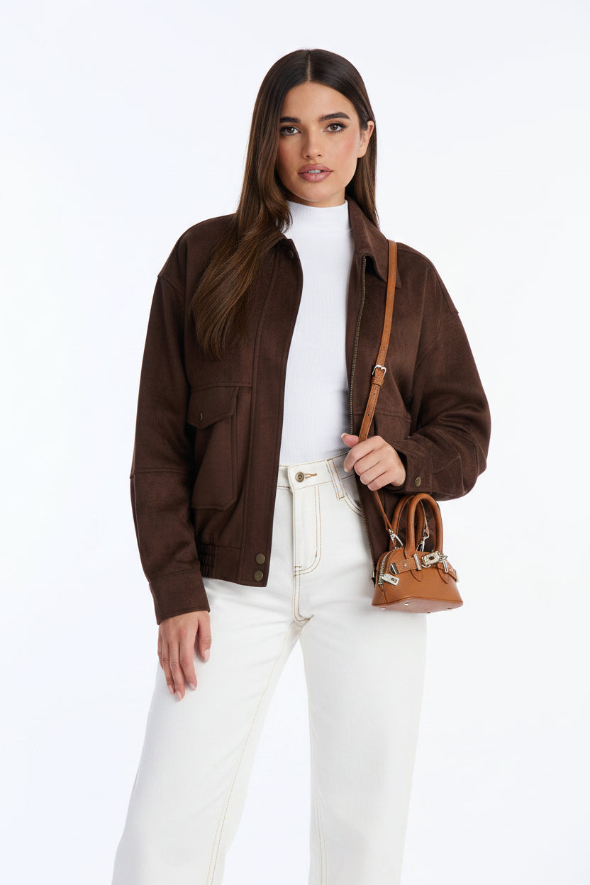 Woman wearing a brown jacket and white pants, holding a brown handbag on a white background