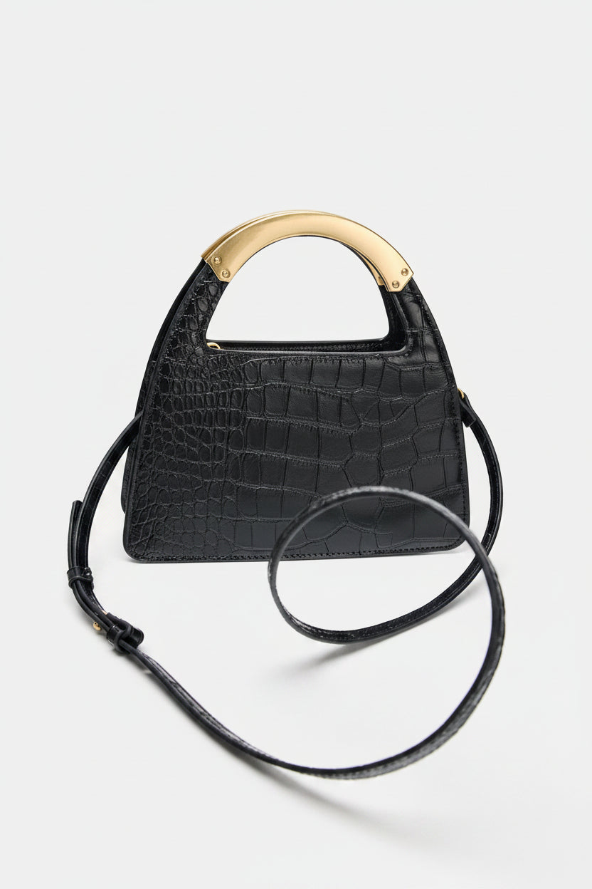 Black crocodile-patterned handbag with a gold handle on a white background