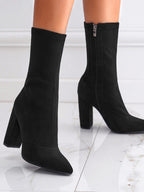 Black sock boots with block heels on a white marble floor