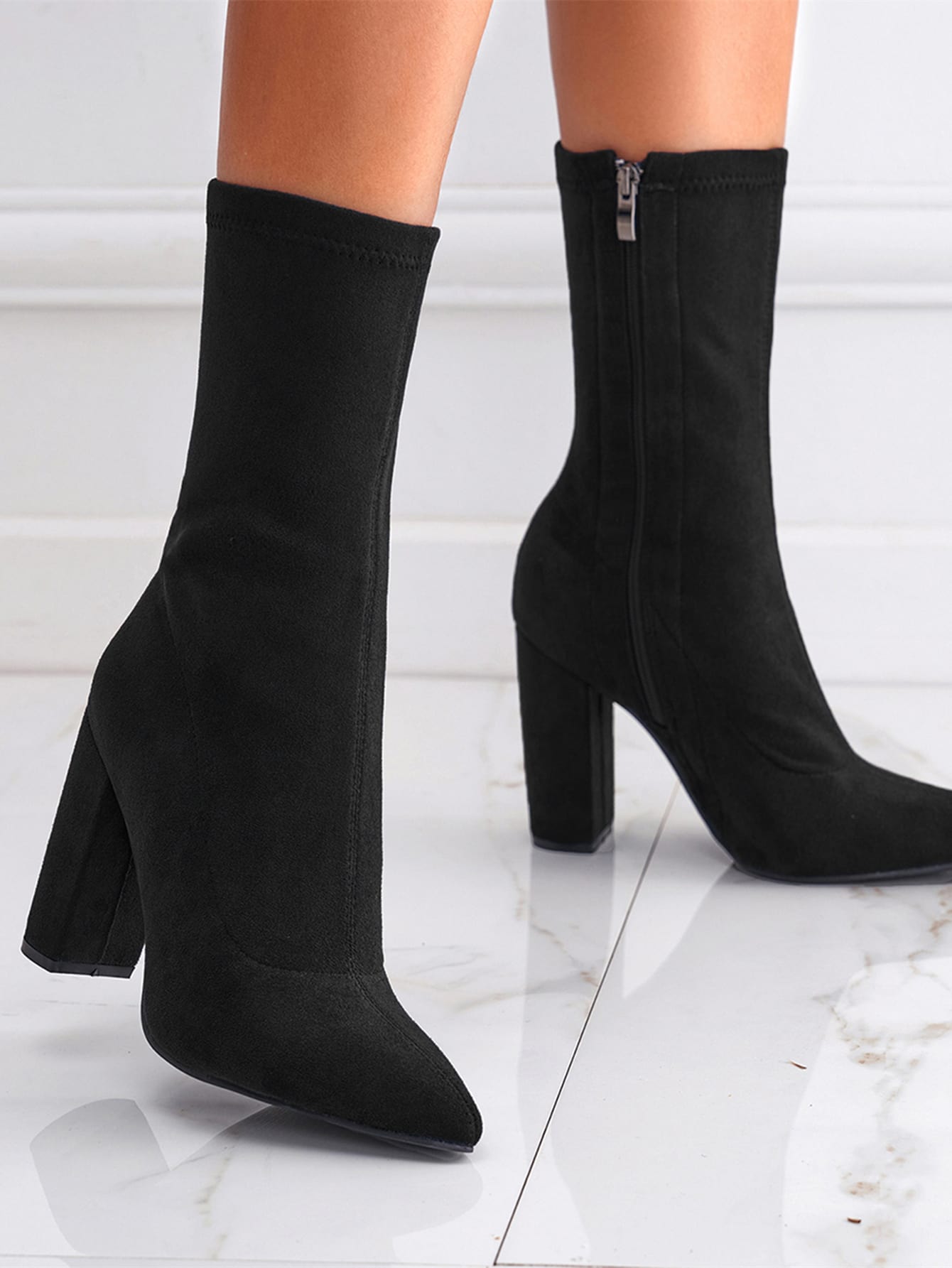 Black sock boots with block heels on a white marble floor