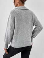 Person wearing a gray knitted sweater and black pants against a white background
