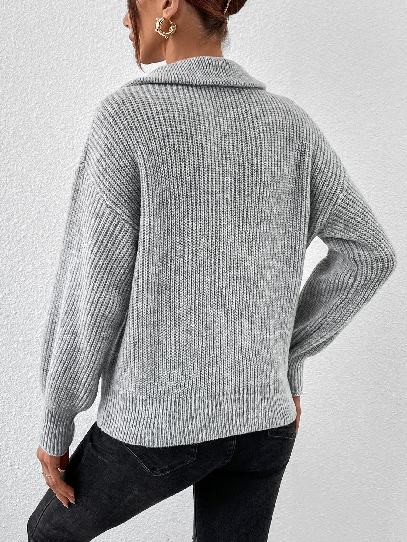 Person wearing a gray knitted sweater and black pants against a white background