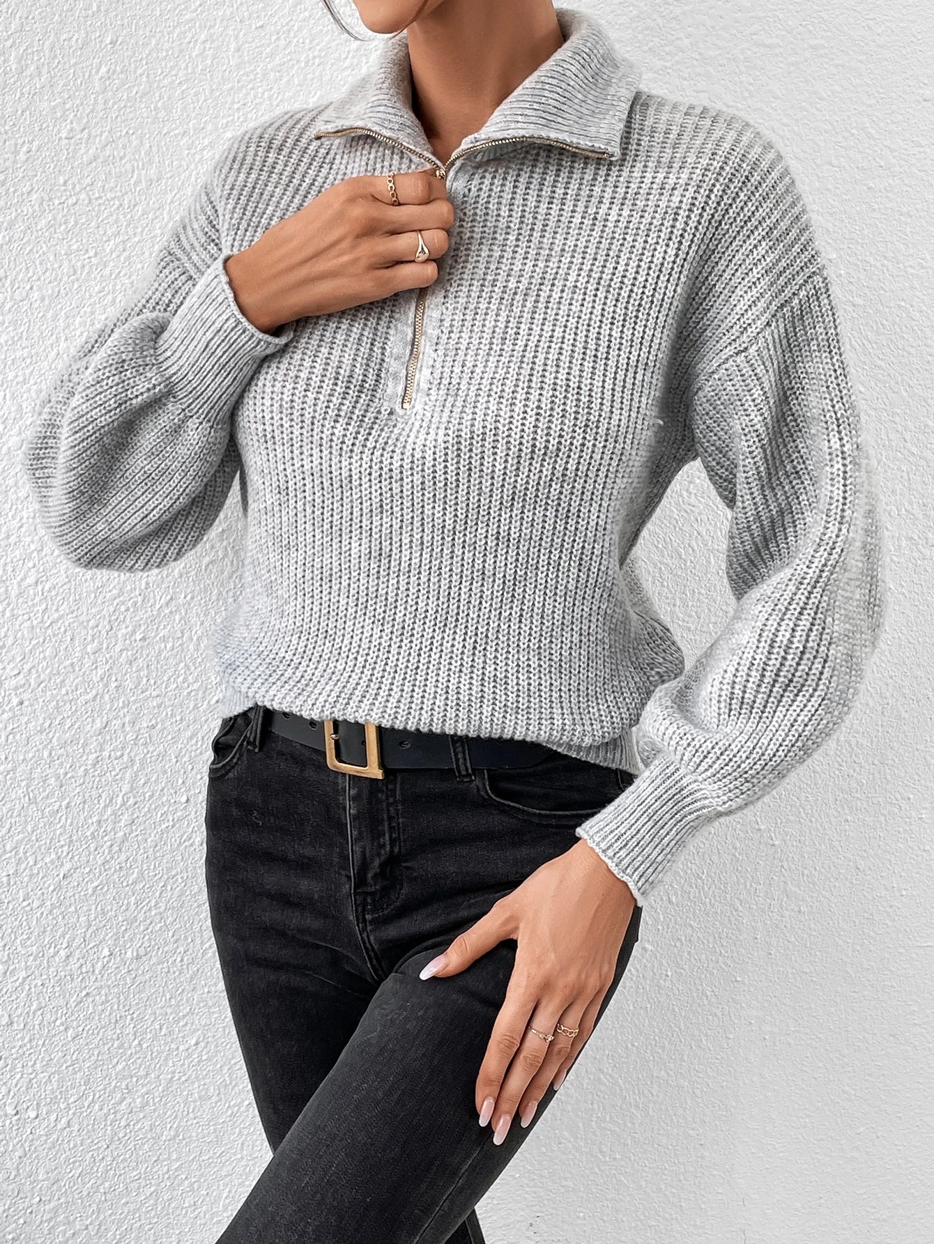 Person wearing a gray knitted sweater and black pants against a white background