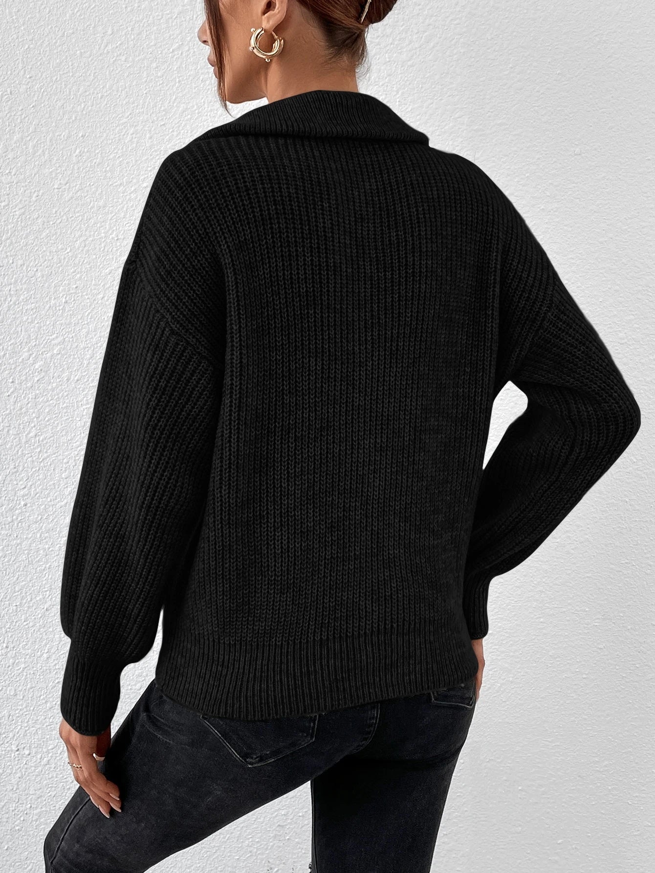Person wearing a black knitted sweater and black pants against a white background