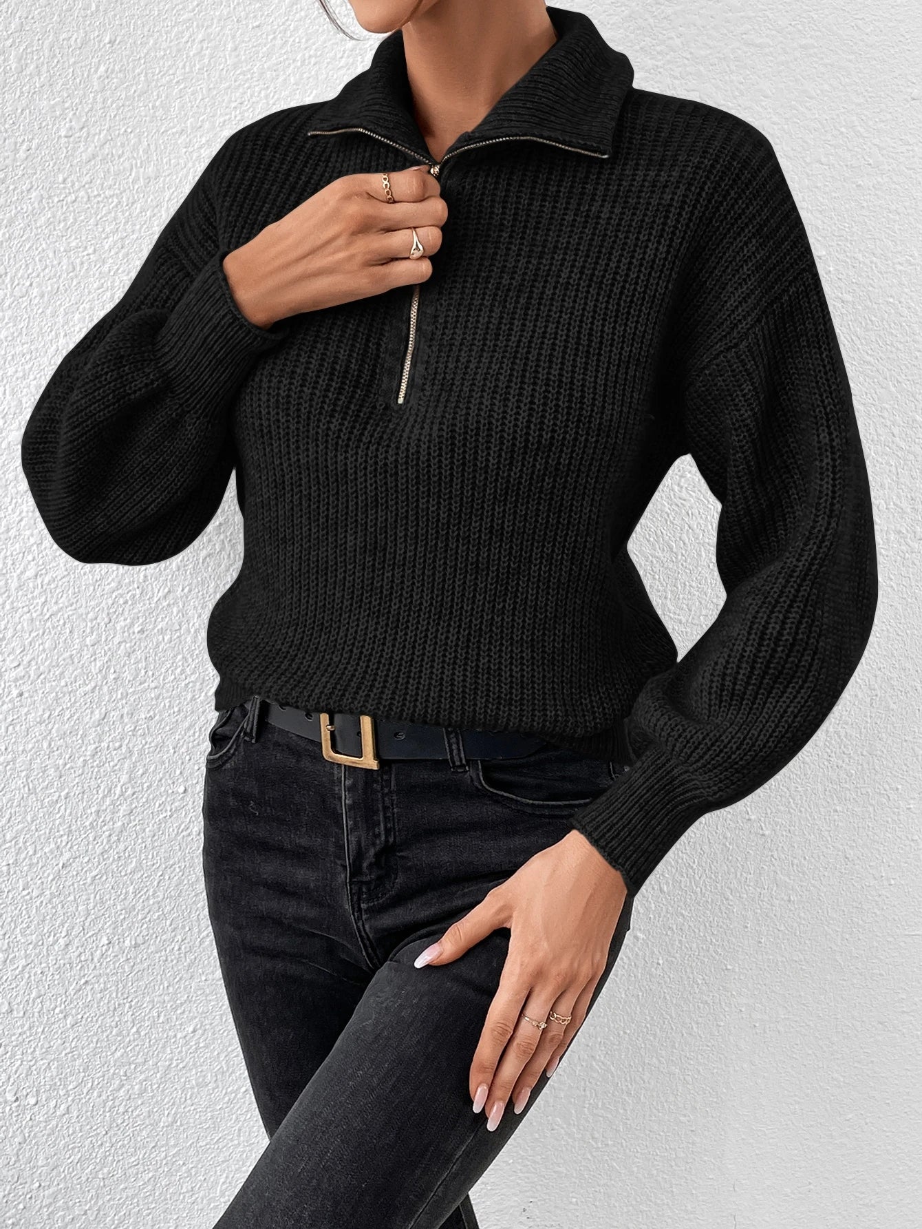 Person wearing a black knitted sweater and black pants against a white background