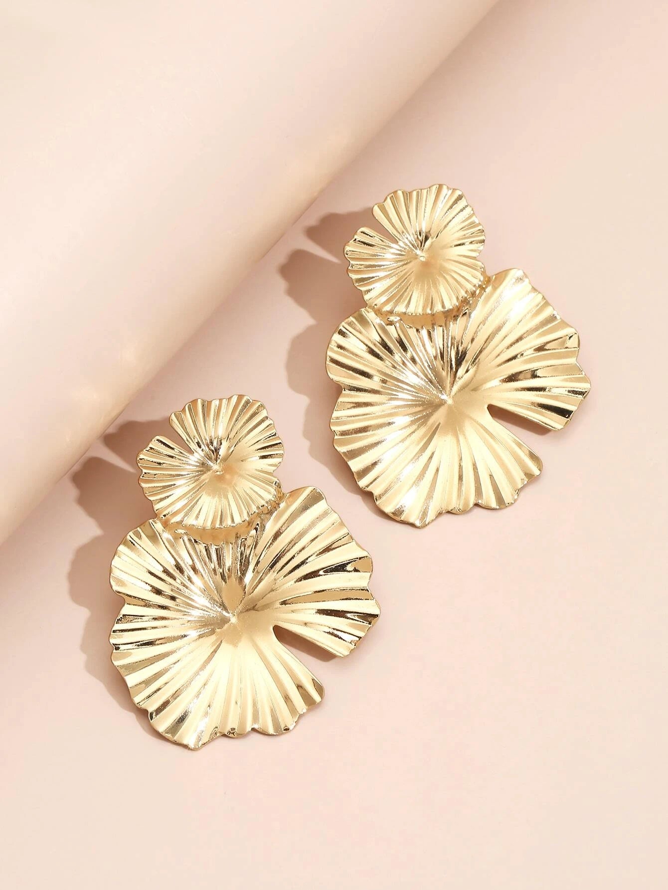 Gold leaf-shaped earrings on a light pink background