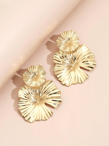 Gold leaf-shaped earrings on a light pink background