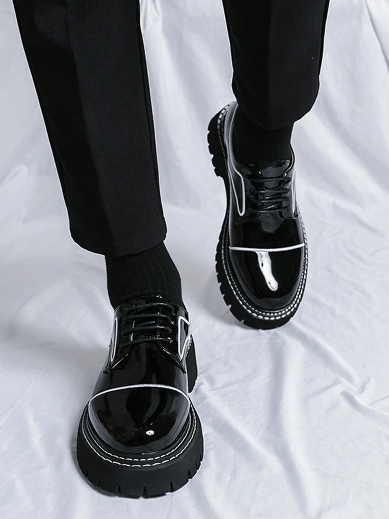 Black glossy shoes worn with black pants on a white background