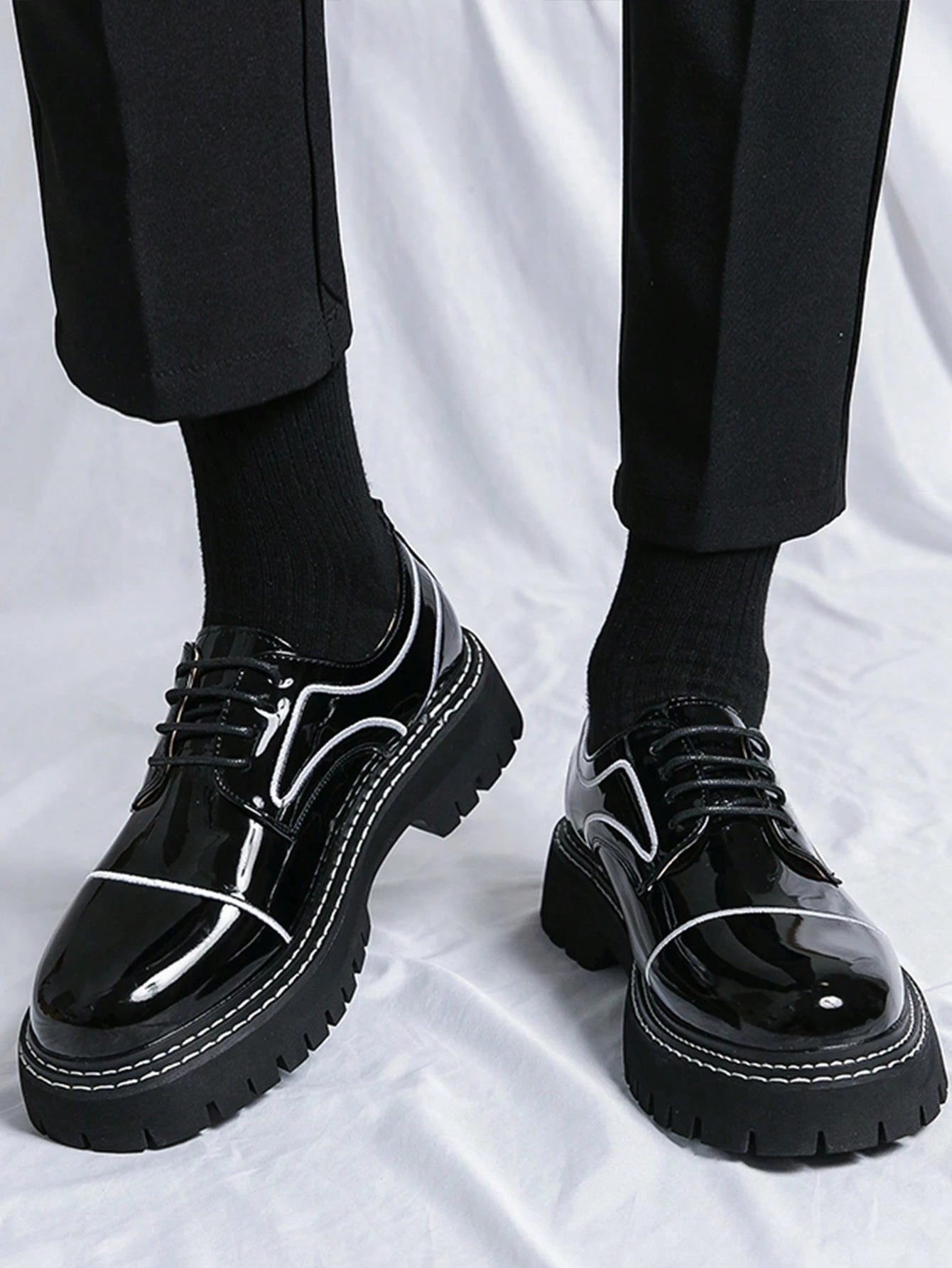 Black glossy shoes with white accents worn with black pants and socks on a white background
