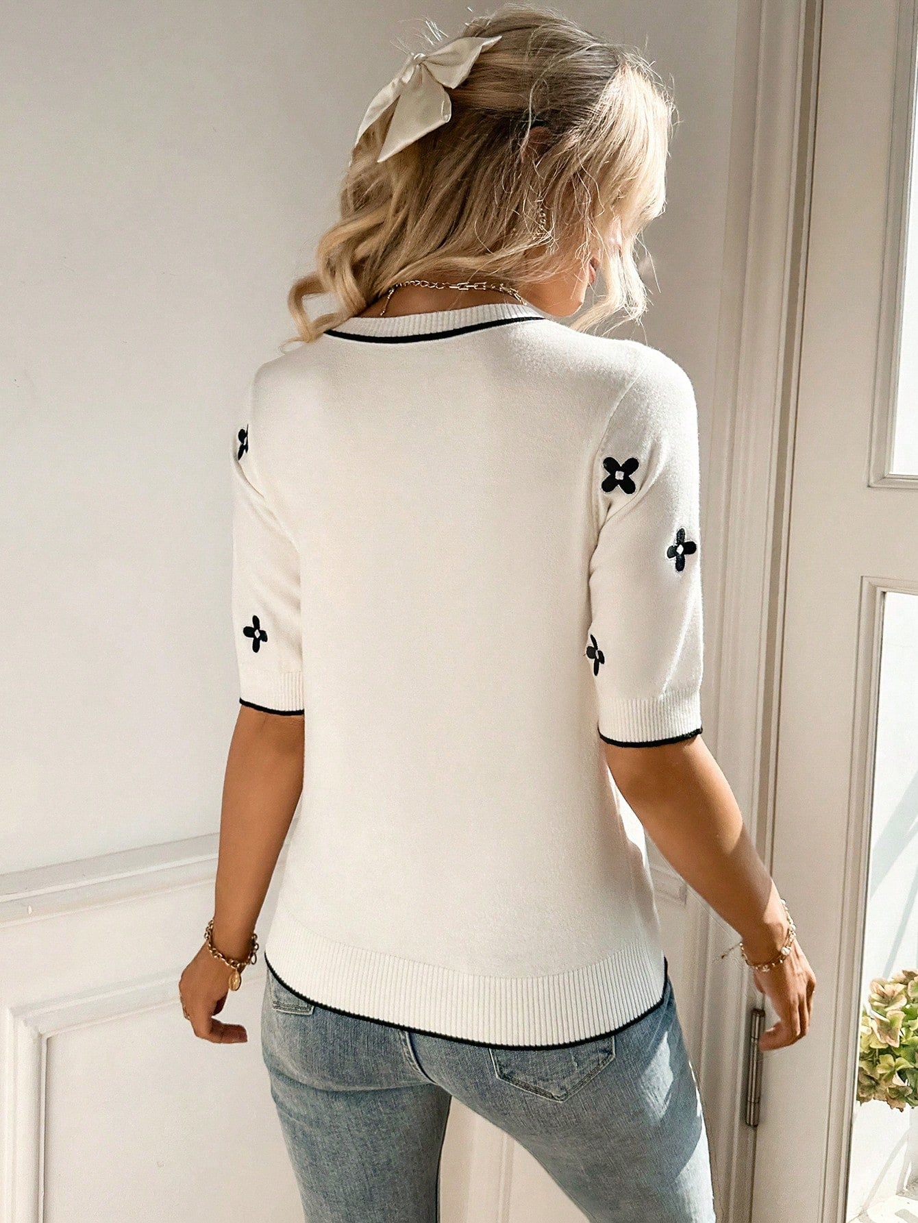 Person wearing a white sweater with black patterns and light blue jeans indoors.