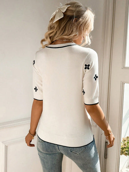Person wearing a white sweater with black patterns and light blue jeans indoors.
