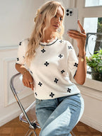 Woman taking a selfie wearing a white top with black patterns and blue jeans indoors.