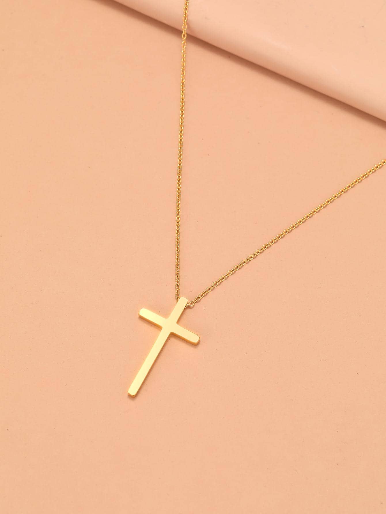 Gold cross necklace on a pink background