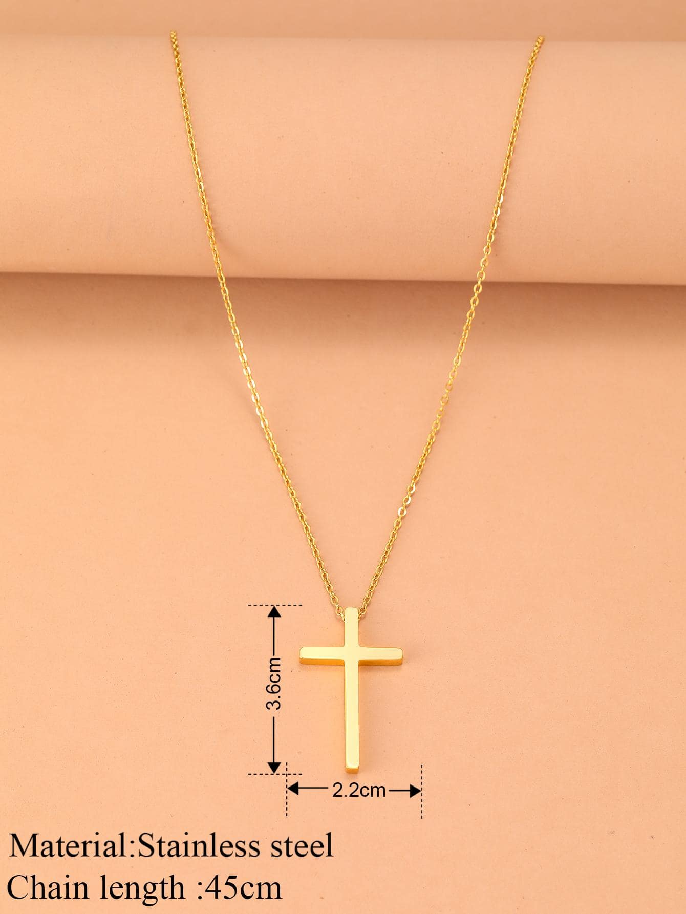 Gold cross necklace with measurements on a pink background