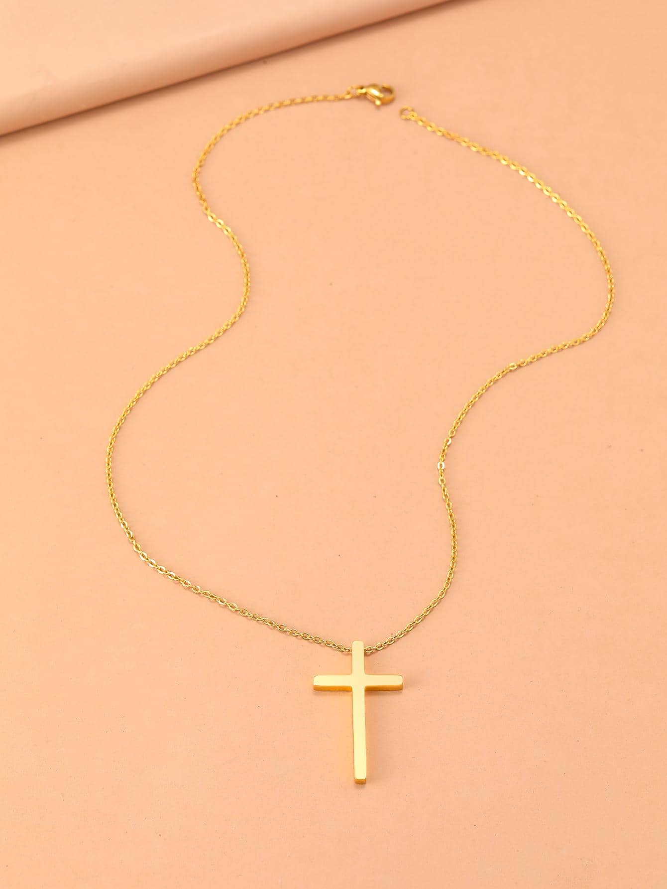 Gold necklace with a cross pendant on a beige background