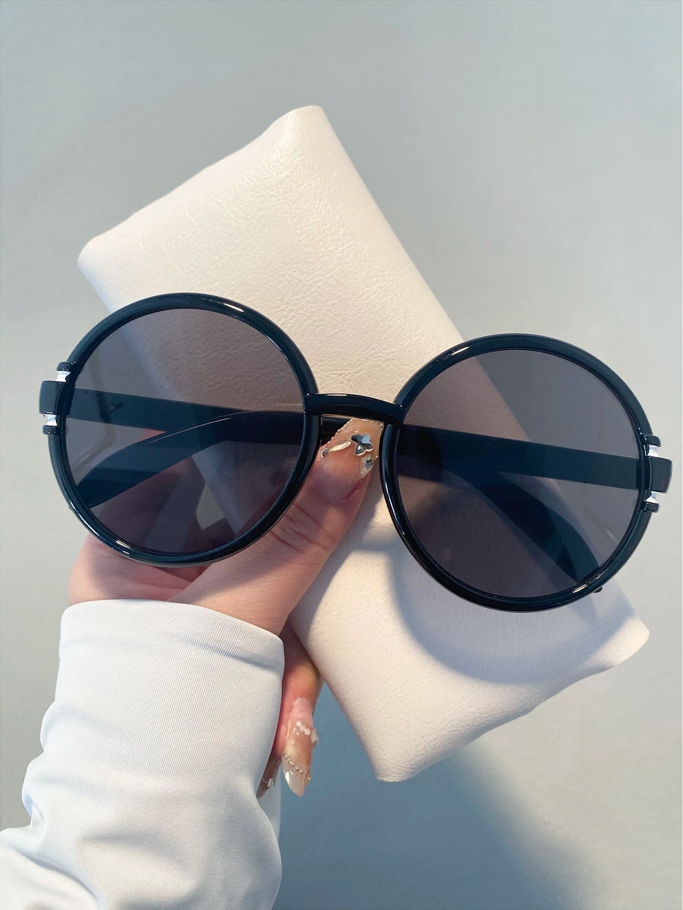 Round black sunglasses held by a hand with a neutral background