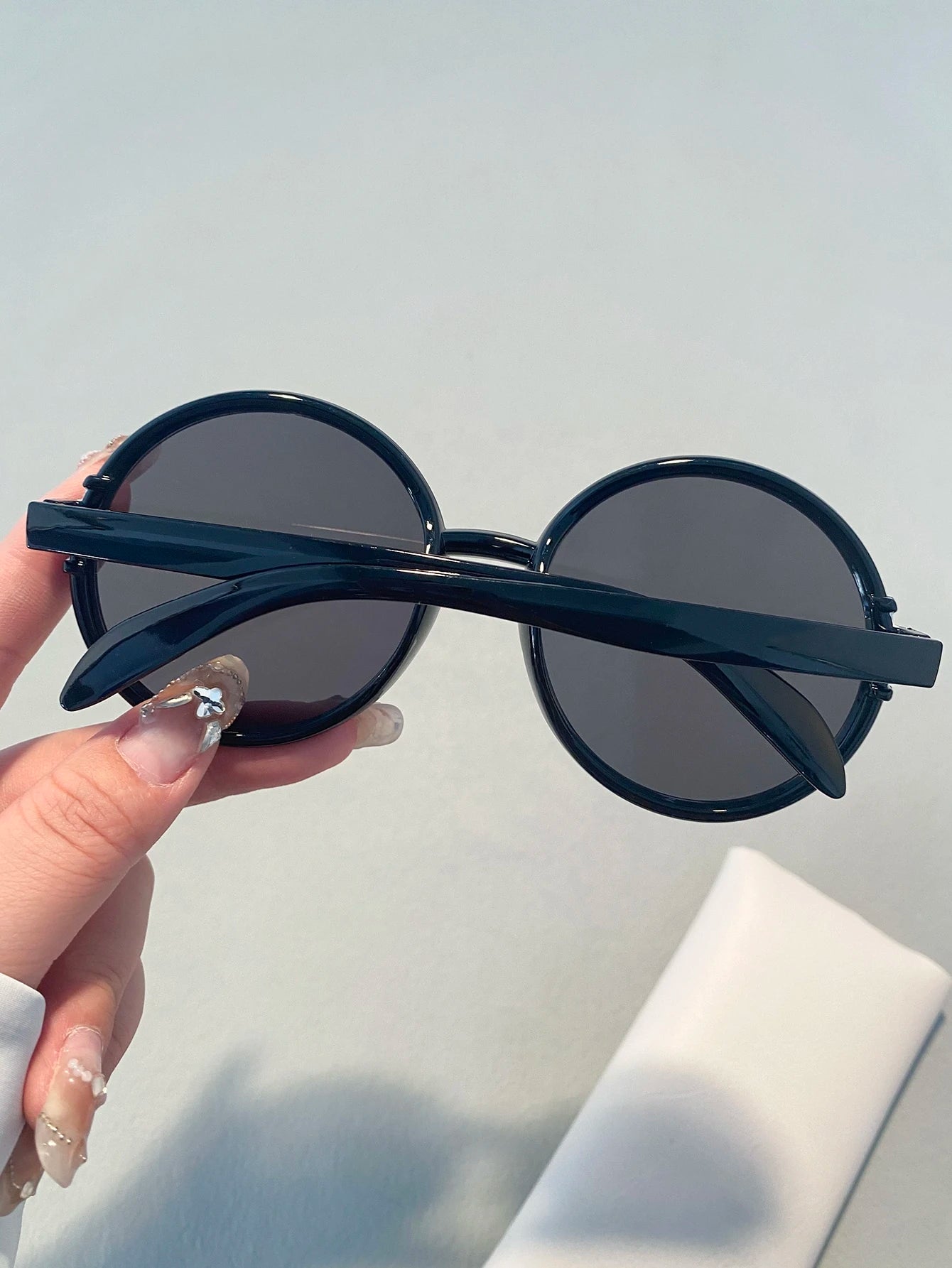 Black round sunglasses held by a hand against a light gray background