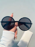 Black round sunglasses held by a hand against a light gray background