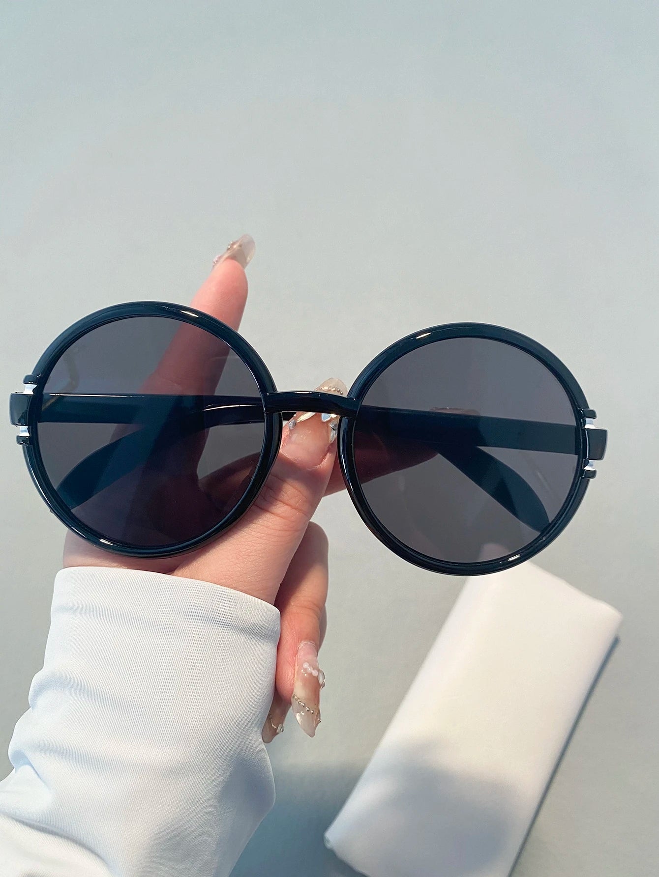 Black round sunglasses held by a hand against a light gray background