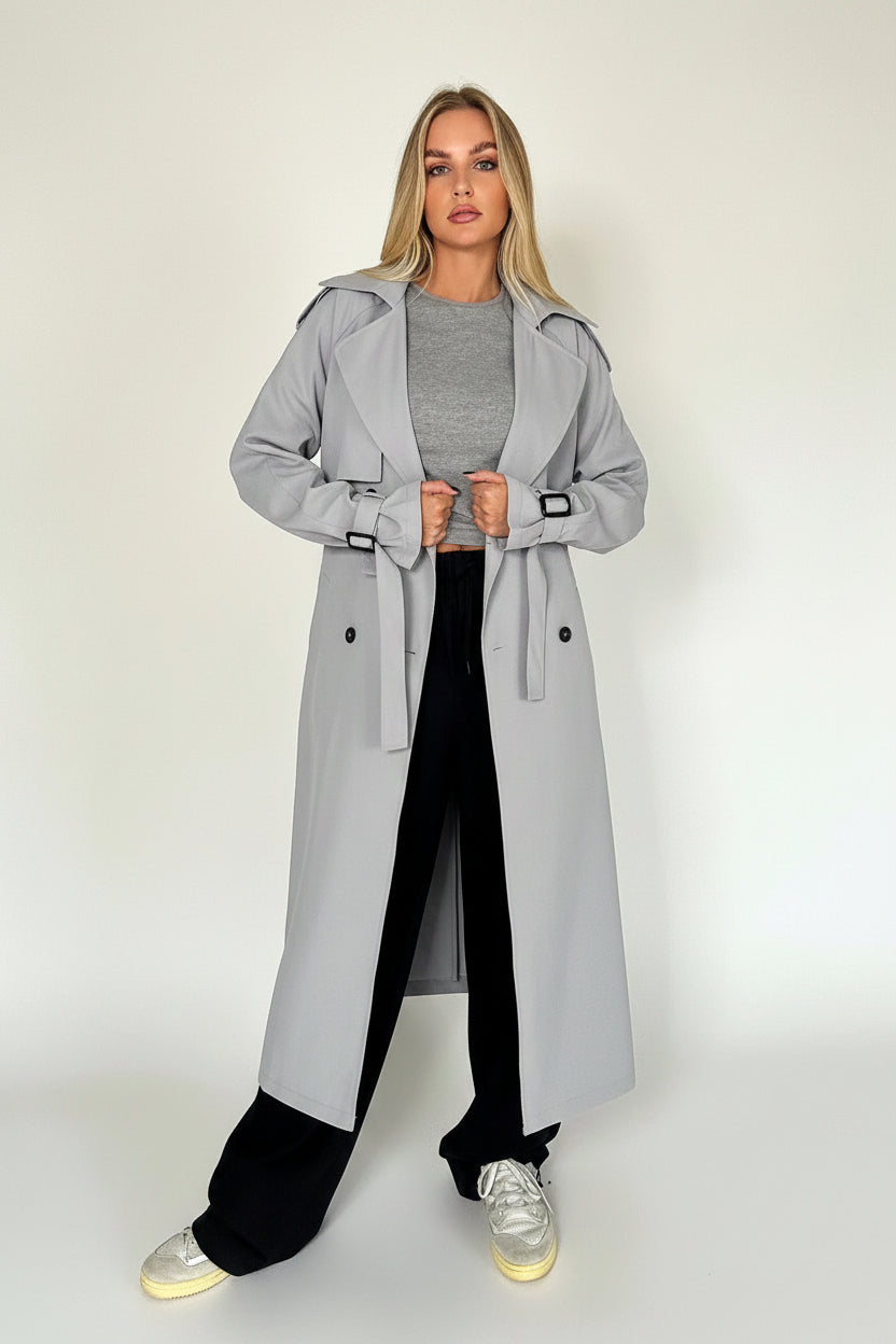 Woman wearing a gray trench coat standing indoors.