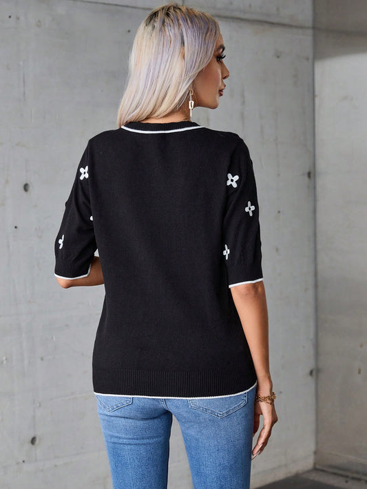 Person wearing a black sweater with white patterns and blue jeans against a gray concrete wall.