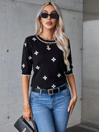 Woman wearing a black top with white patterns and blue jeans against a gray concrete wall.