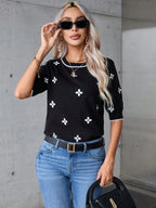 Woman wearing a black sweater with white patterns and blue jeans, standing against a concrete wall.