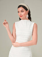 Woman wearing a white textured dress with a tiara and earrings against a plain background