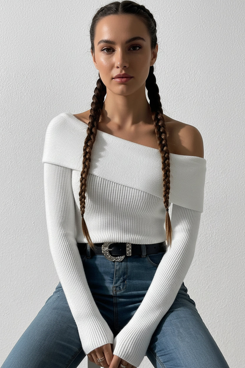 Person wearing a white off-shoulder sweater and blue jeans against a plain background