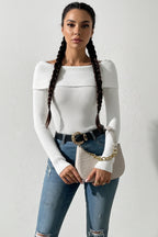 Person wearing a white off-shoulder sweater and blue jeans against a plain background
