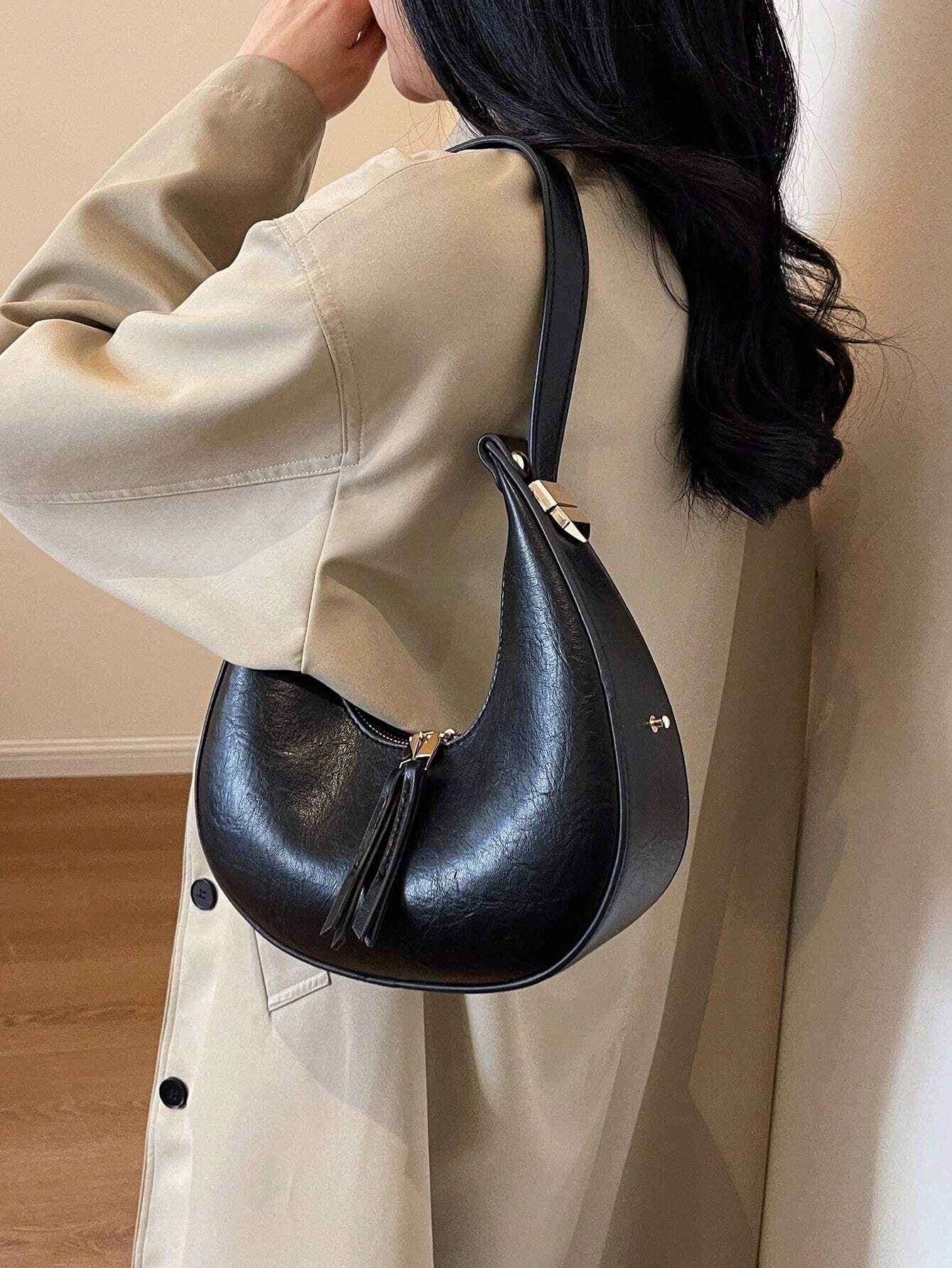 Person wearing a beige coat with a black handbag featuring a tassel.