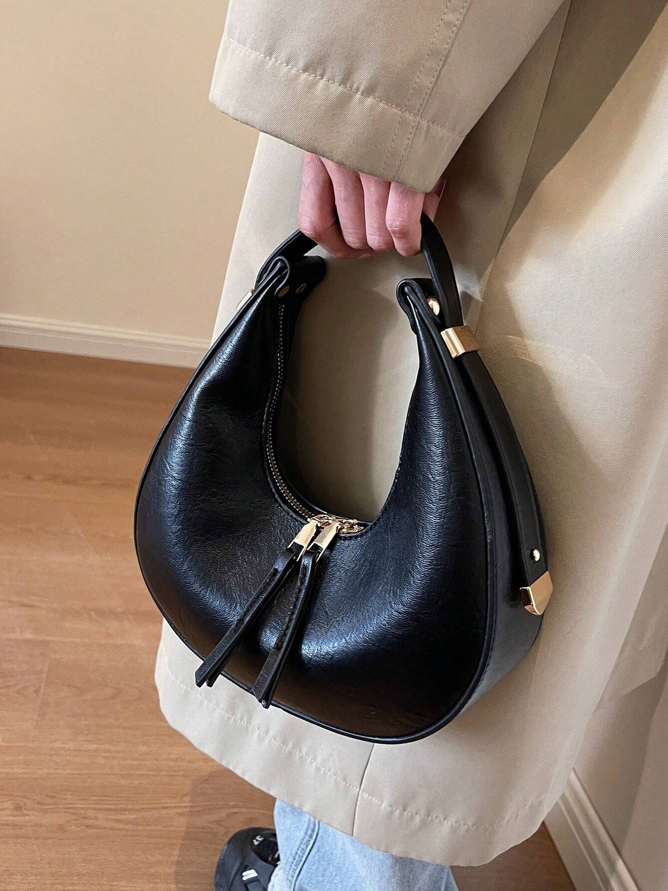 Person holding a black handbag with gold accents indoors