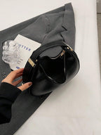 Black handbag on a white surface with a gray jacket and a glass bottle.