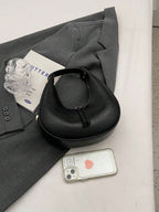 Black handbag on a gray surface with a phone and a glass bottle.