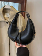 Black handbag held in front of a beige coat with a visible brand tag.
