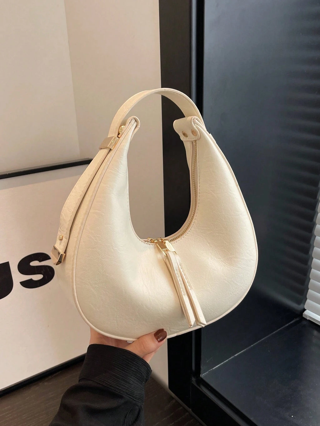 Beige handbag held by a person in front of a black and white background