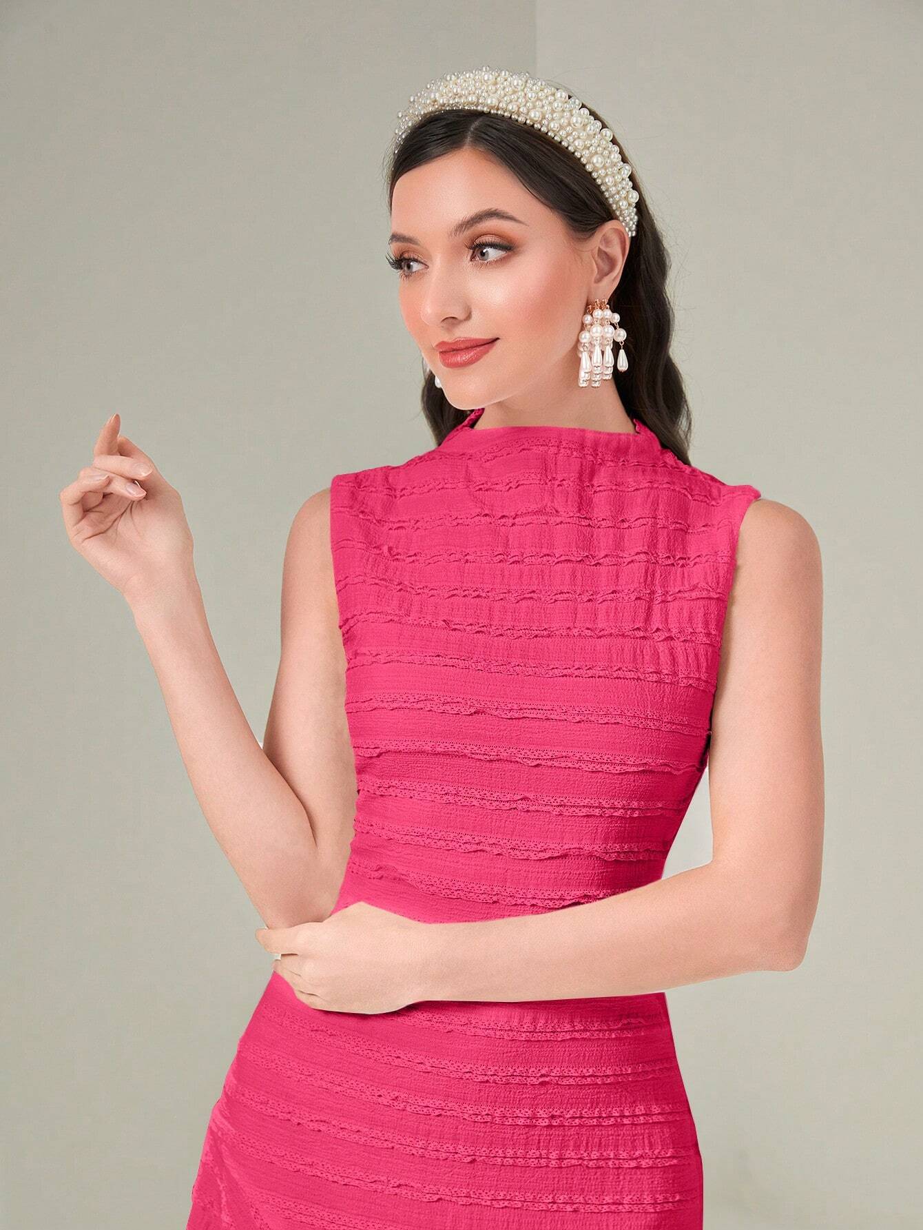 Woman wearing a pink dress with a tiara and earrings on a plain background