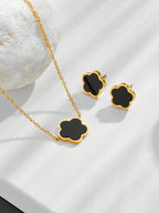 Gold necklace and earrings with black clover-shaped pendants on a white background