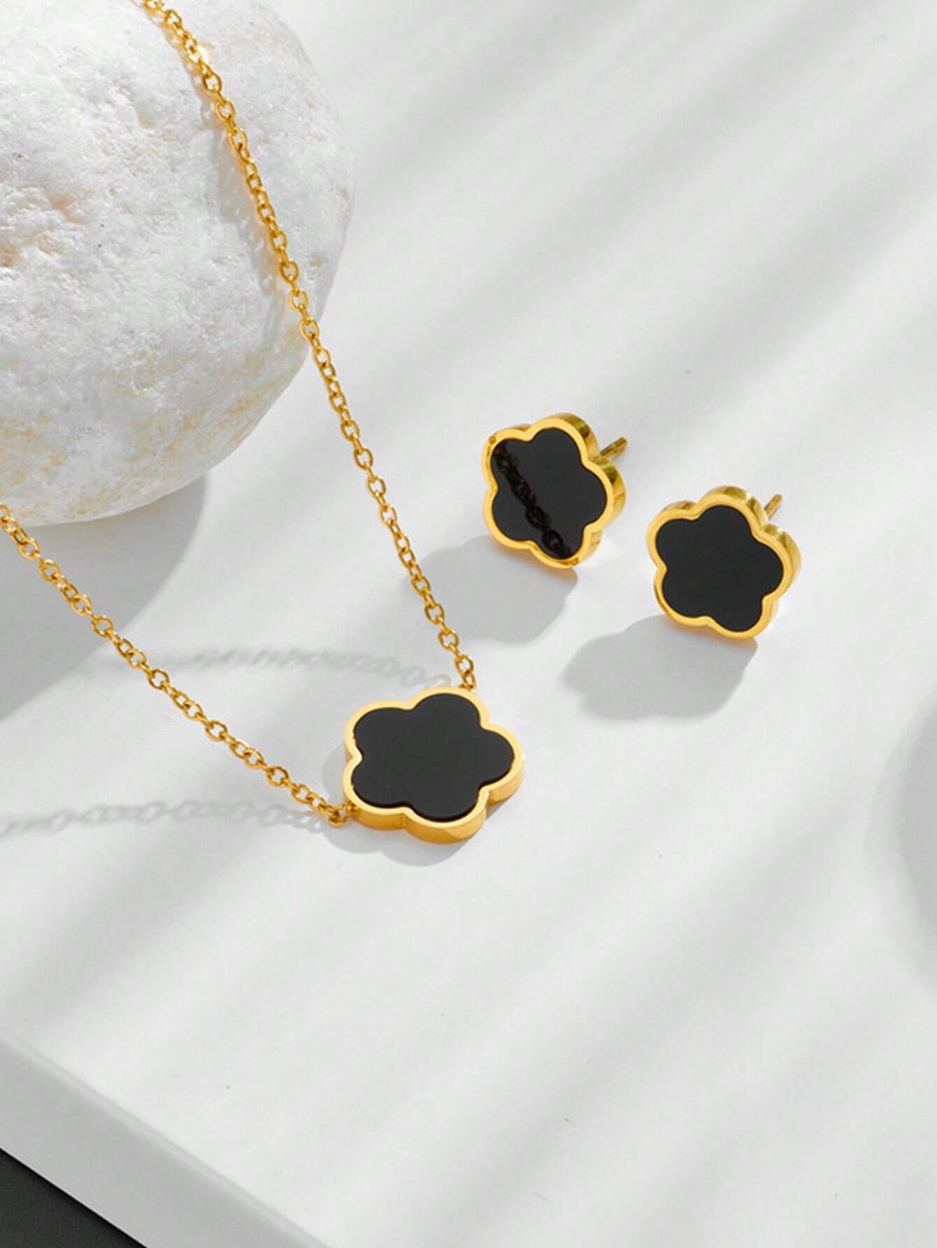 Gold necklace and earrings with black clover-shaped pendants on a white background