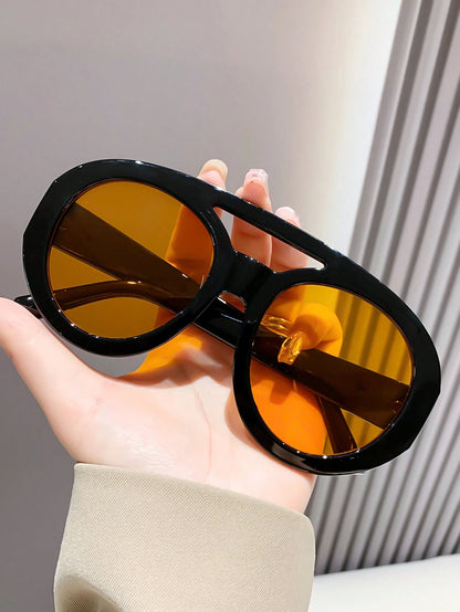 Sunglasses with black frame and yellow lenses held by a hand against a neutral background