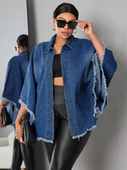 Woman wearing a blue denim jacket with fringe details, black sunglasses, and black pants against a gray background.