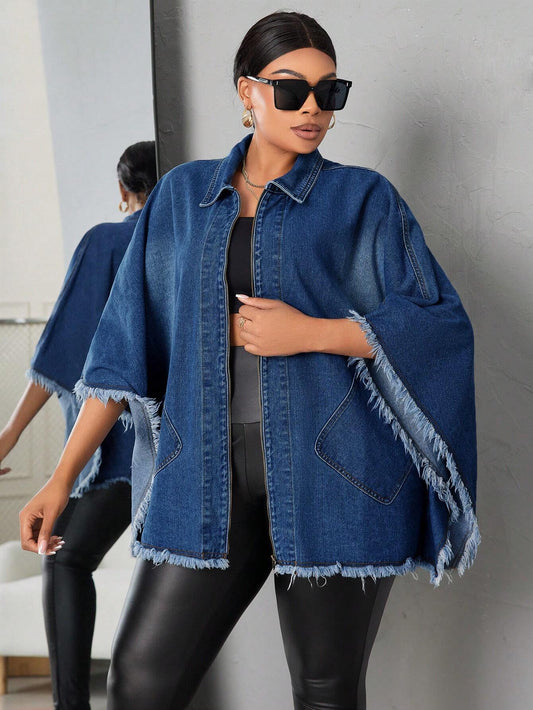 Woman wearing a blue denim jacket with a fringe detail, black sunglasses, and black pants against a gray wall.