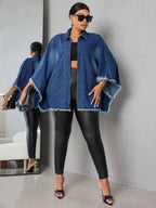 Woman wearing a blue denim jacket and black leggings standing against a gray wall.