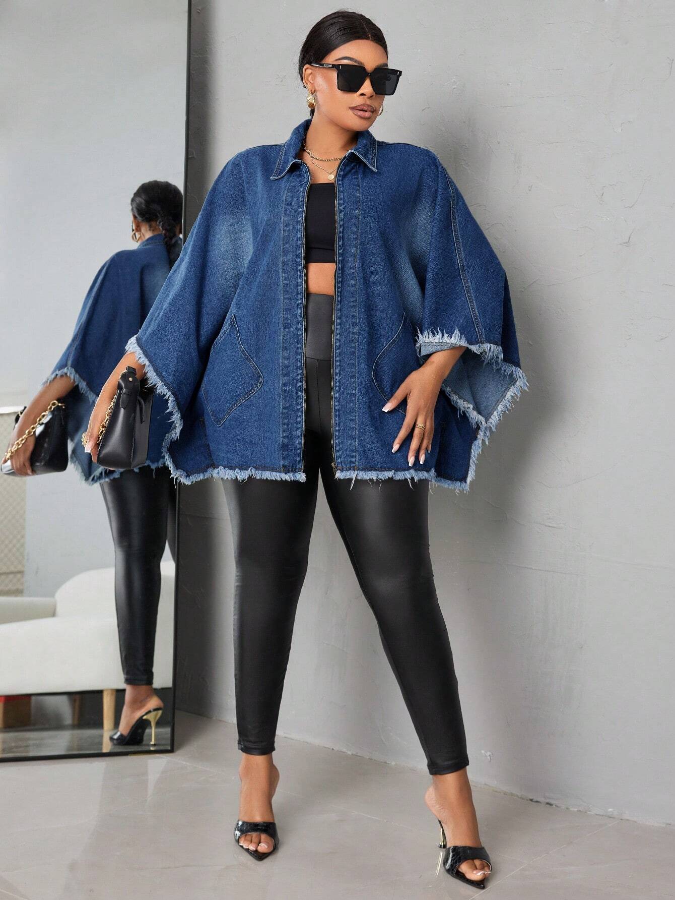 Woman wearing a blue denim jacket and black leggings standing against a gray wall.